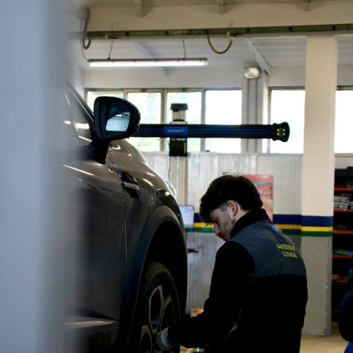 Mechanic adjusting car tire on lift in an indoor workshop setting.